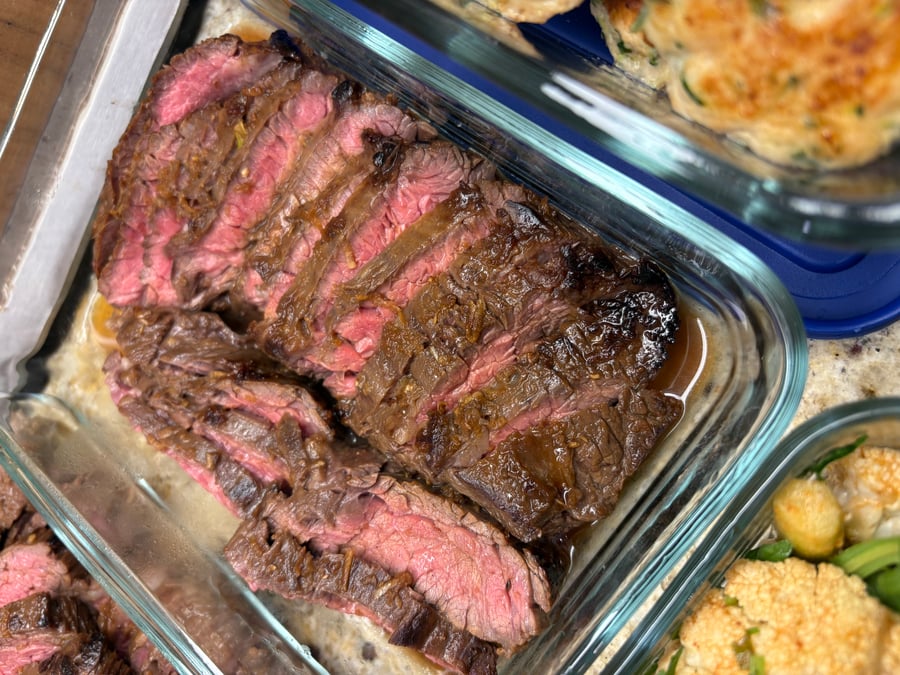 A glass storage container holding thinly sliced Vietnamese skirt steak with a vibrant pink interior, served in a lime agave vinaigrette glaze.