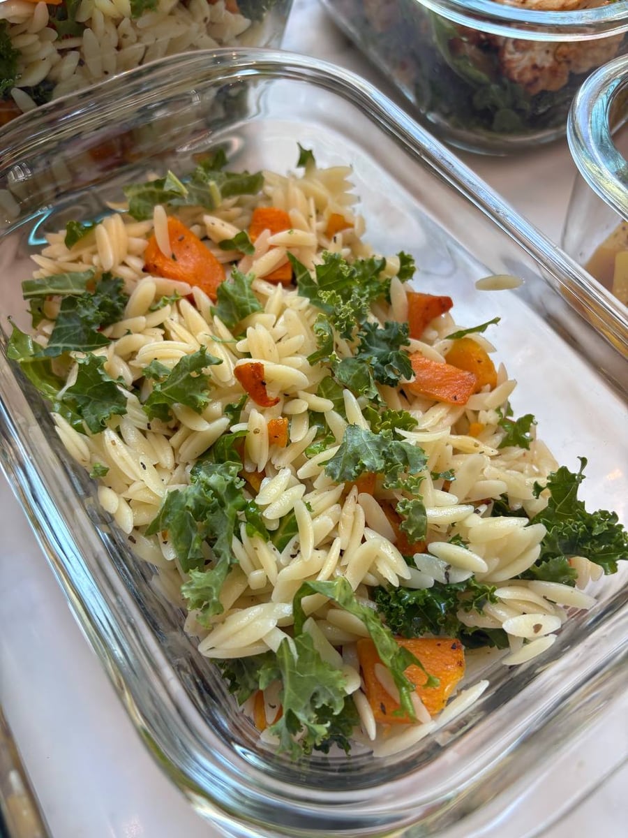Glass meal prep containers showing orange glazed chicken bites, butternut squash kale brown rice orzo, and feta roasted beets served in clear square dishes.