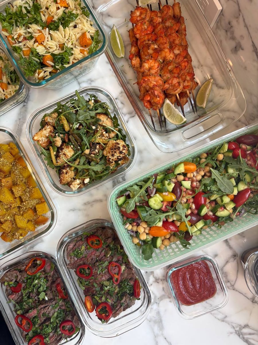 Glass containers filled with paprika shrimp, Vietnamese flank steak, roasted golden beets, orzo with butternut squash, and a fresh Mediterranean chickpea vegetable salad.