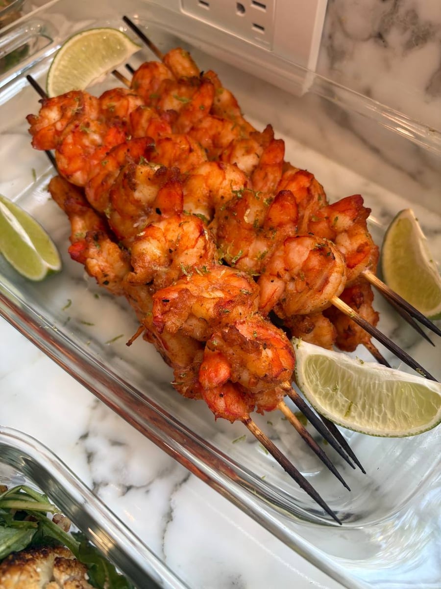 A glass container filled with vibrant paprika-dusted grilled shrimp skewers, garnished with fresh lime wedges and a light sprinkling of citrus zest.