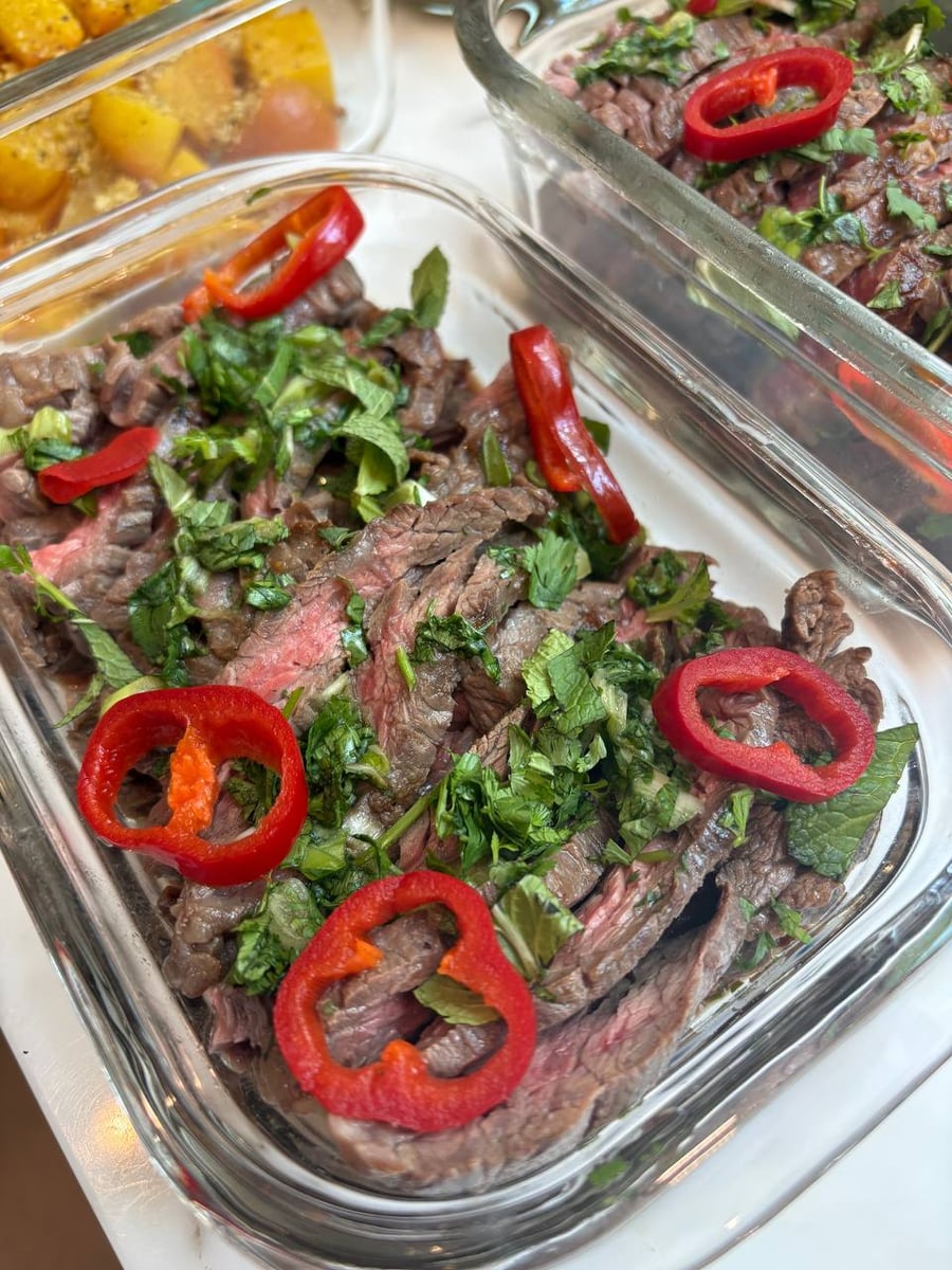 Glass meal prep containers filled with thin-sliced Vietnamese flank steak topped with fresh chopped herbs and vibrant red chili pepper rings.