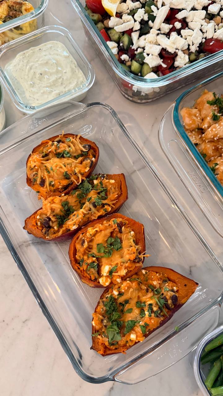 A glass dish features four halved sweet potatoes stuffed with a blend of black beans, cottage cheese, and herbs, arranged neatly for service.