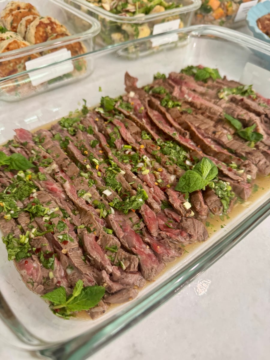 A glass serving dish filled with thinly sliced Vietnamese flank steak topped with a fresh herb and lime vinaigrette in a bright kitchen.