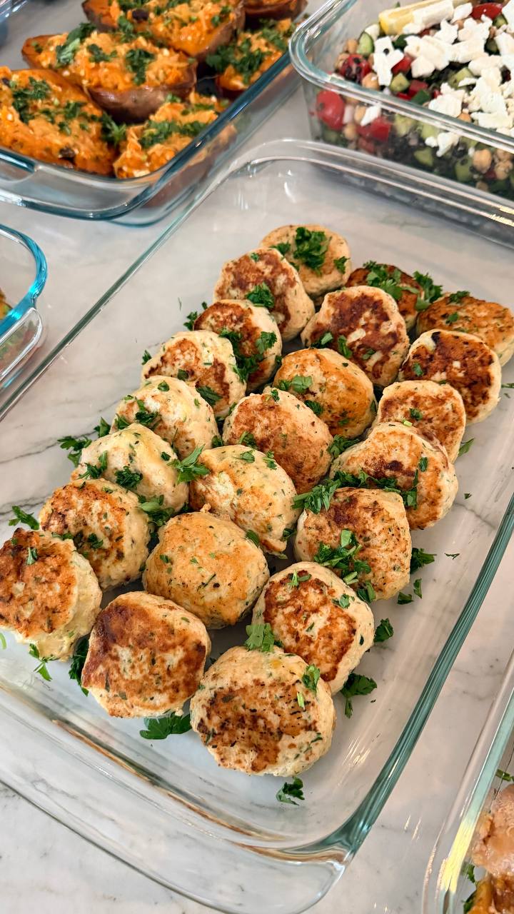 A glass baking dish filled with golden-brown zucchini turkey fritters, garnished with fresh green parsley and arranged in neat rows for easy serving.