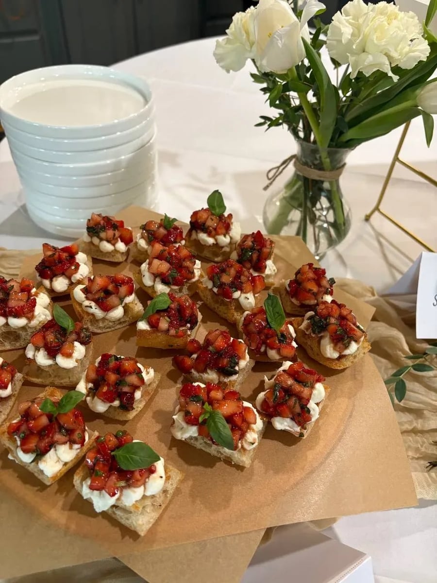 Close-up of whipped ricotta crostini topped with balsamic strawberry and fresh basil leaves on parchment.
