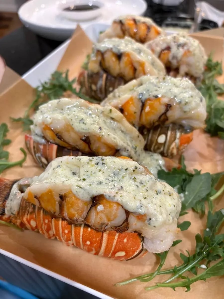 Butter-poached lobster tails with herb beurre blanc sauce, plated on parchment with fresh arugula.