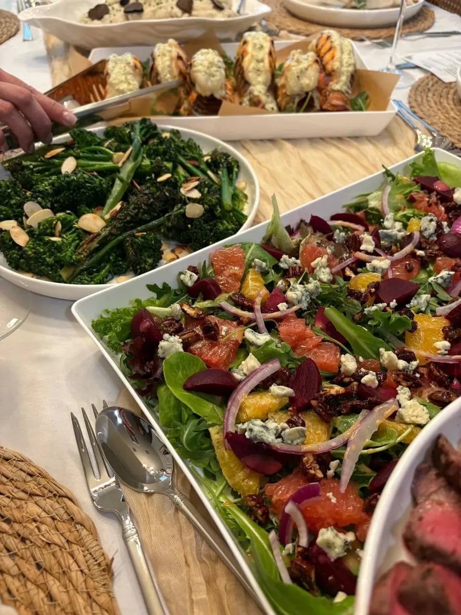 Family-style dinner table with baby greens and citrus salad, charred broccolini with almonds, and butter-poached lobster tails.