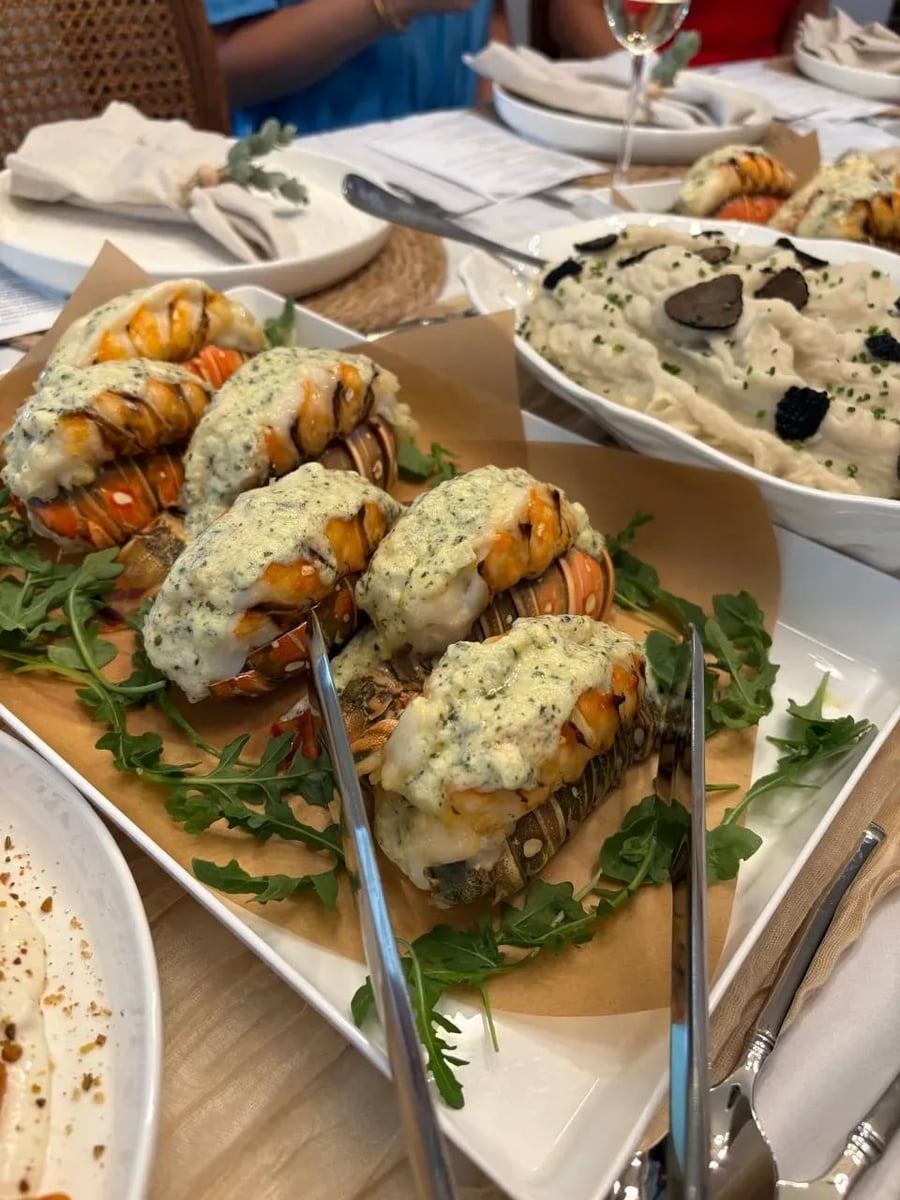 Butter-poached lobster tails with herb beurre blanc being served at the dinner table, truffle potato purée visible in background.