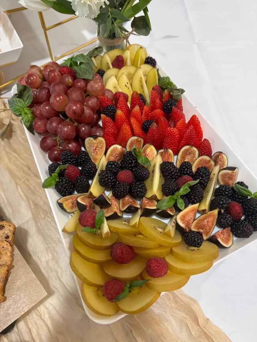Elegant fruit board with red grapes, strawberries, figs, blackberries, raspberries, and golden kiwi slices.