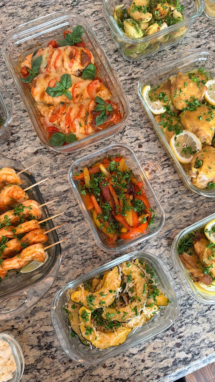 A variety of meal prep glass containers featuring tomato basil caprese chicken, saffron turmeric chicken, paprika lime shrimp, acorn squash, and roasted brussels sprouts.