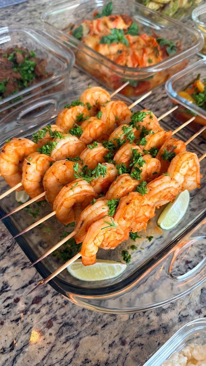 Grilled paprika lime shrimp skewers arranged in a glass rectangular dish, garnished with fresh chopped parsley and served with vibrant lime wedges.