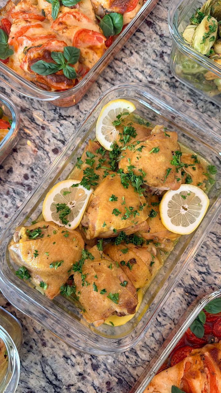 A glass container features golden saffron turmeric baked chicken thighs garnished with fresh lemon slices and chopped parsley, served alongside Caprese chicken and Brussels sprouts.