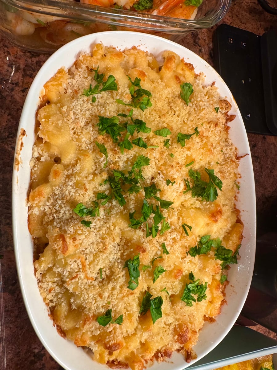 A white oval baking dish filled with golden baked macaroni and cheese, topped with a crunchy panko breadcrumb crust and fresh green parsley garnish.