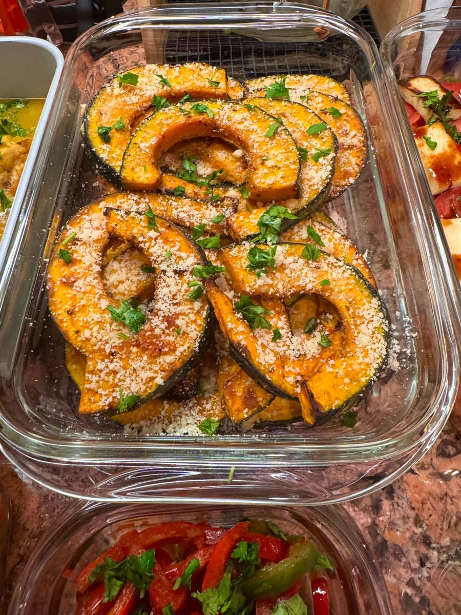 These perfectly roasted acorn squash wedges are elegantly presented in a clear glass container, showcasing their deep golden-orange flesh and charred edges.