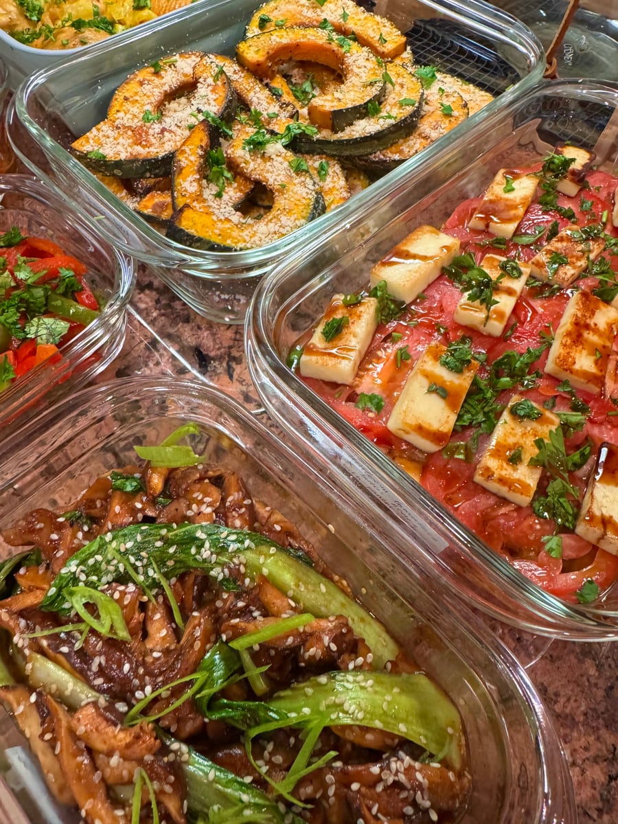 A collection of glass containers holding roasted acorn squash, tomato and grilled halloumi salad, and sesame chicken with bok choy for a healthy meal selection.