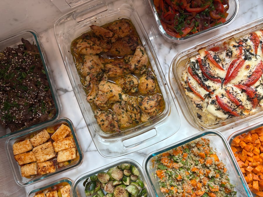 A collection of glass meal prep containers featuring saffron chicken, tomato basil chicken, Chinese beef stir-fry, roasted sweet potatoes, quinoa, Brussels sprouts, and fajita vegetables.