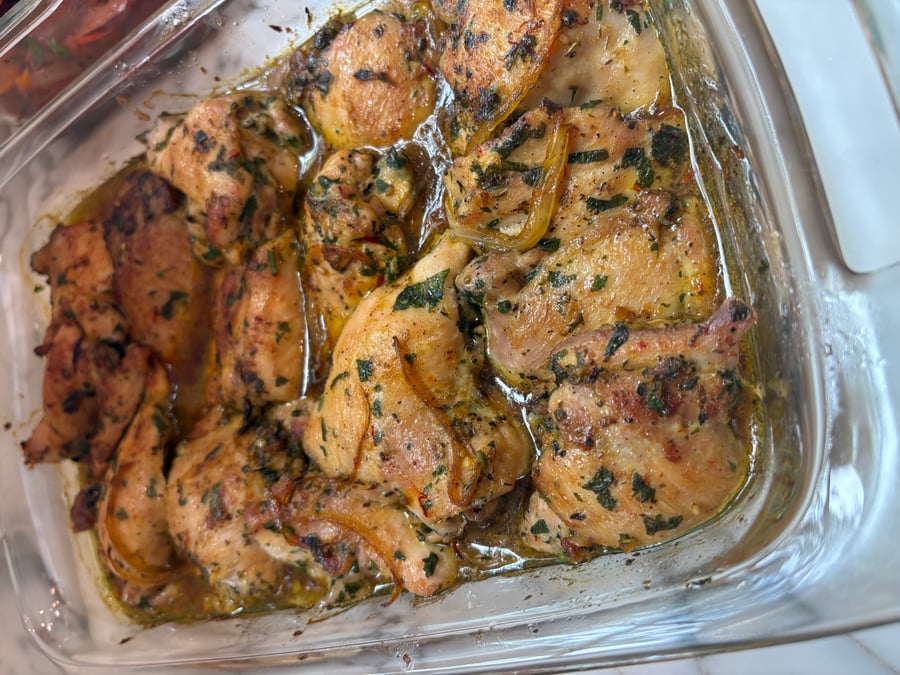 A glass baking dish filled with golden-brown saffron turmeric baked chicken thighs, seasoned with fresh herbs and cooked in a savory pan sauce.