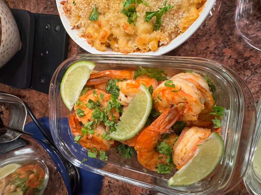These savory, pan-seared shrimp are beautifully presented with a vibrant garnish of fresh cilantro and lime wedges alongside a hearty portion of baked pasta.