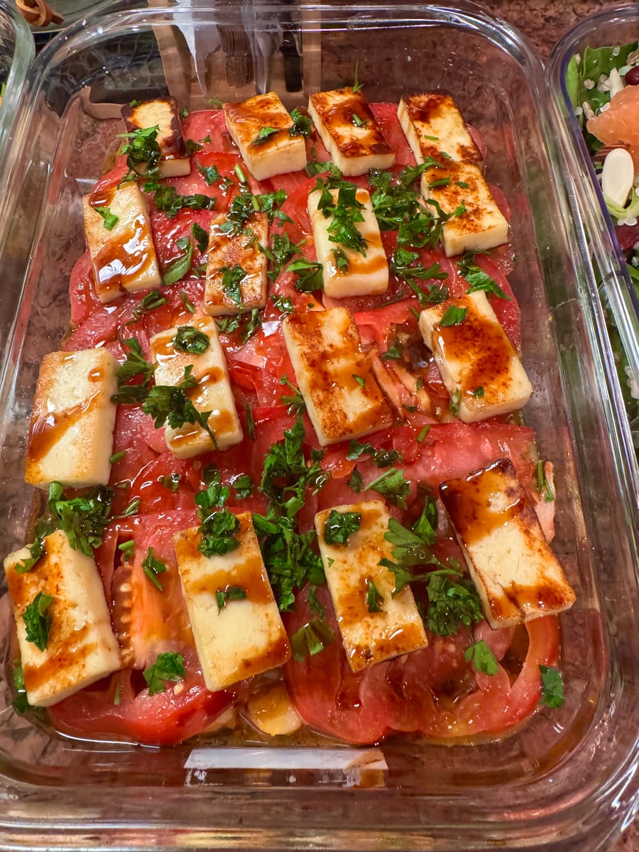 This glass tray is layered with thick slices of fresh tomatoes topped with golden seared halloumi cheese, fresh chopped parsley, and a balsamic glaze.