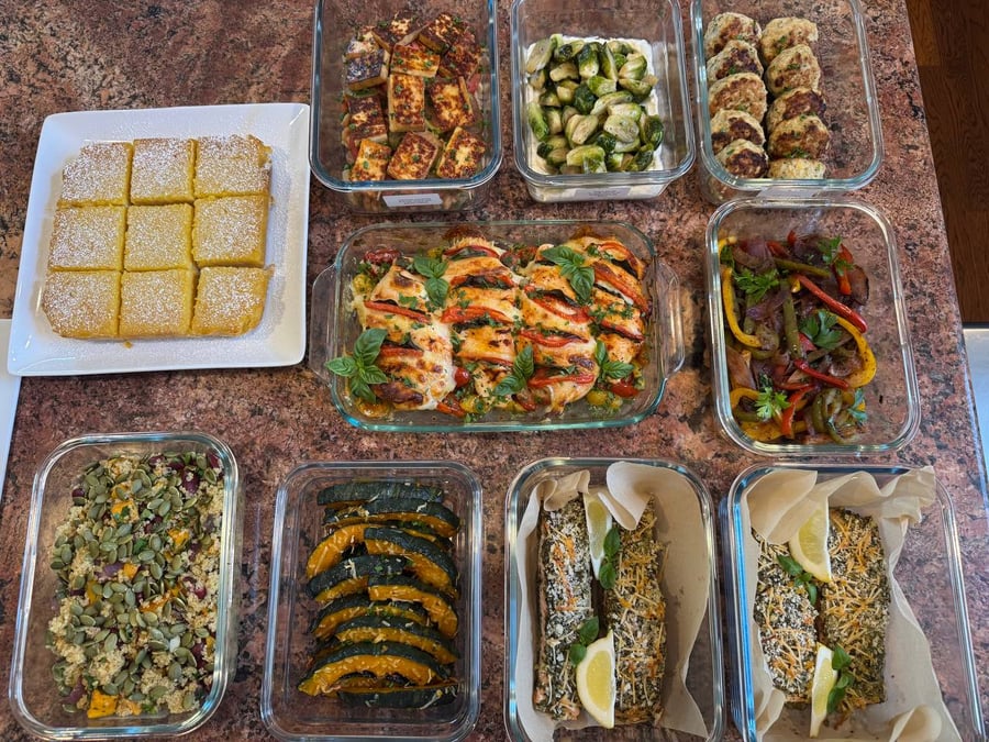 A variety of gourmet dishes including pesto salmon, tomato basil chicken, roasted vegetables, and lemon bars neatly arranged in glass food storage containers.