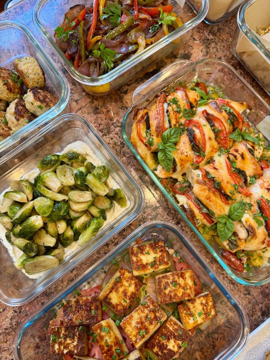 Glass containers holding turkey fritters, tomato basil chicken, roasted Brussels sprouts on whipped feta, and heirloom tomatoes with crispy paneer cheese.