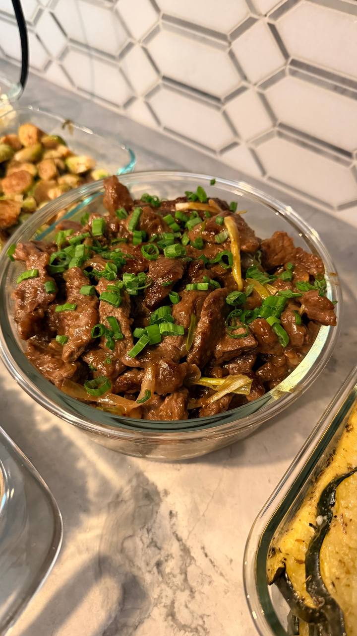 A glass bowl filled with savory Chinese beef and onion stir fry, garnished with vibrant green chopped chives and served in a clear container.