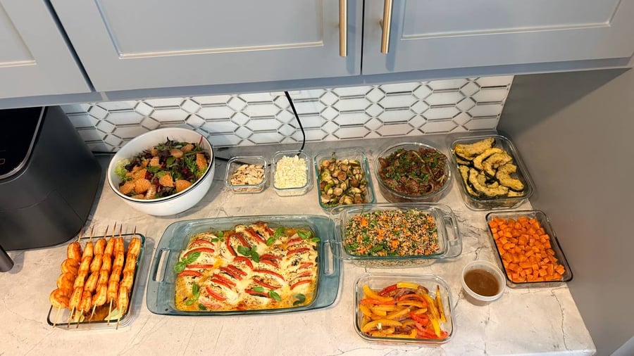 An assortment of meal prep containers featuring tomato basil chicken, paprika shrimp skewers, roasted sweet potatoes, fajita peppers, and a fresh citrus salad.