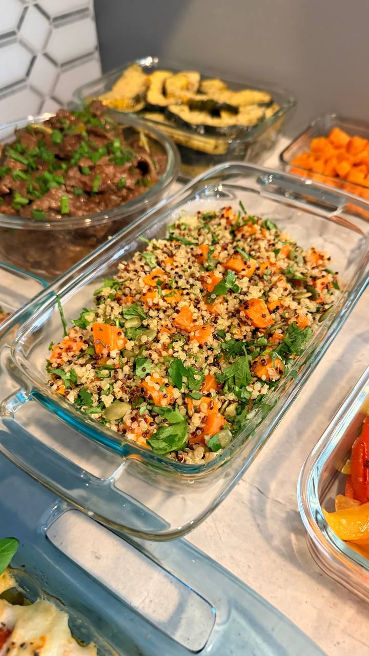 A glass container features roasted sweet potato and cilantro quinoa, alongside containers of beef stir fry, parmesan acorn squash, and roasted fajita vegetables.