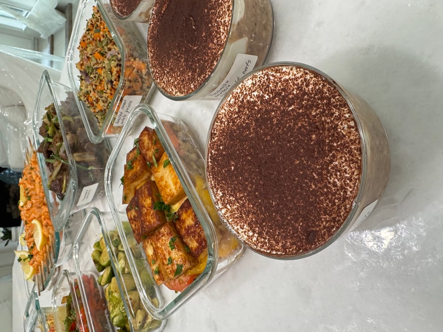 An assortment of glass meal prep containers featuring paneer and heirloom tomatoes, roasted quinoa, shrimp skewers, beef stir fry, Brussels sprouts, and tiramisu oats.