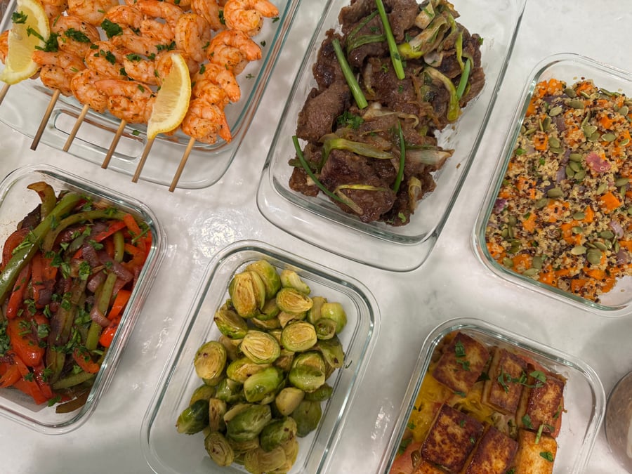Glass meal prep containers filled with paprika lime shrimp, Chinese beef stir fry, masala brussel sprouts, roasted sweet potato quinoa, and paneer cheese.