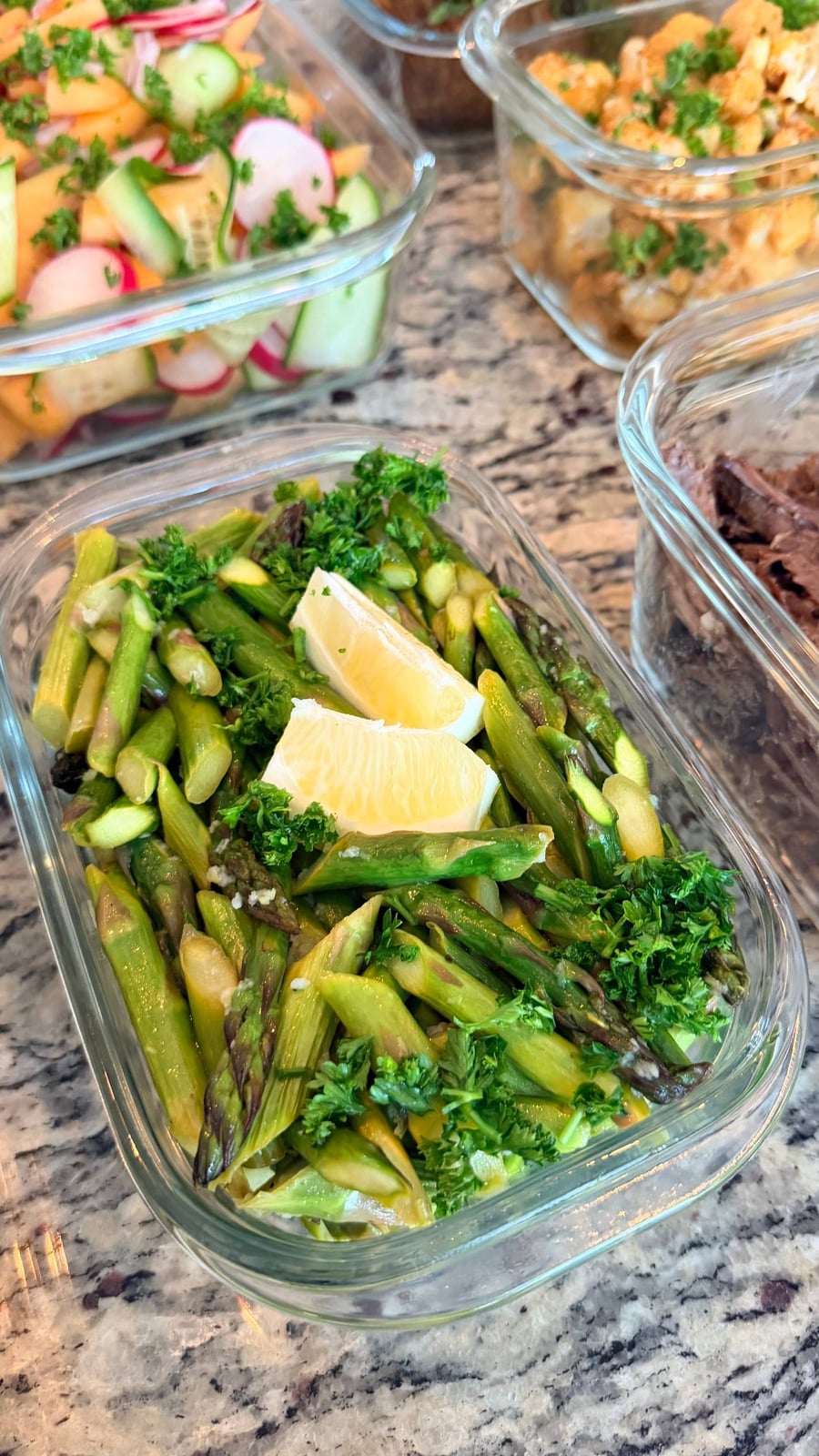 A glass container filled with sautéed ginger garlic asparagus, garnished with fresh parsley and two generous lemon wedges for a vibrant finish.