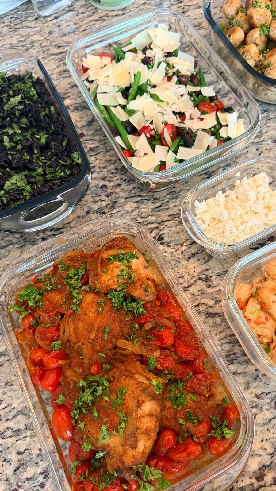 A glass container features zaatar seasoned chicken thighs nestled among roasted cherry tomatoes, garnished with fresh parsley and served in a clear rectangular dish.