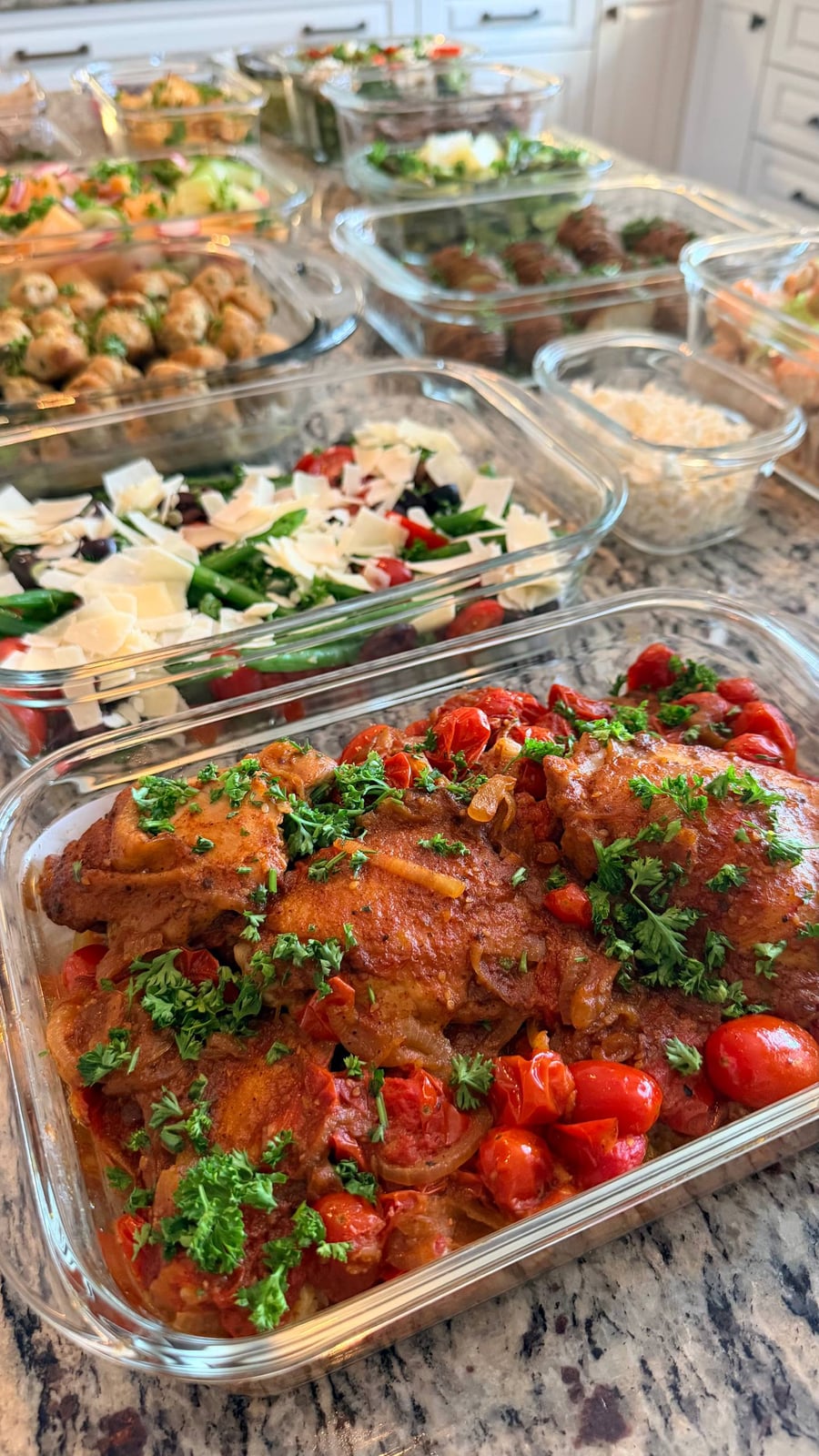 A glass container filled with savory zaatar roast chicken thighs, blistered cherry tomatoes, and fresh green parsley garnish set on a granite countertop.