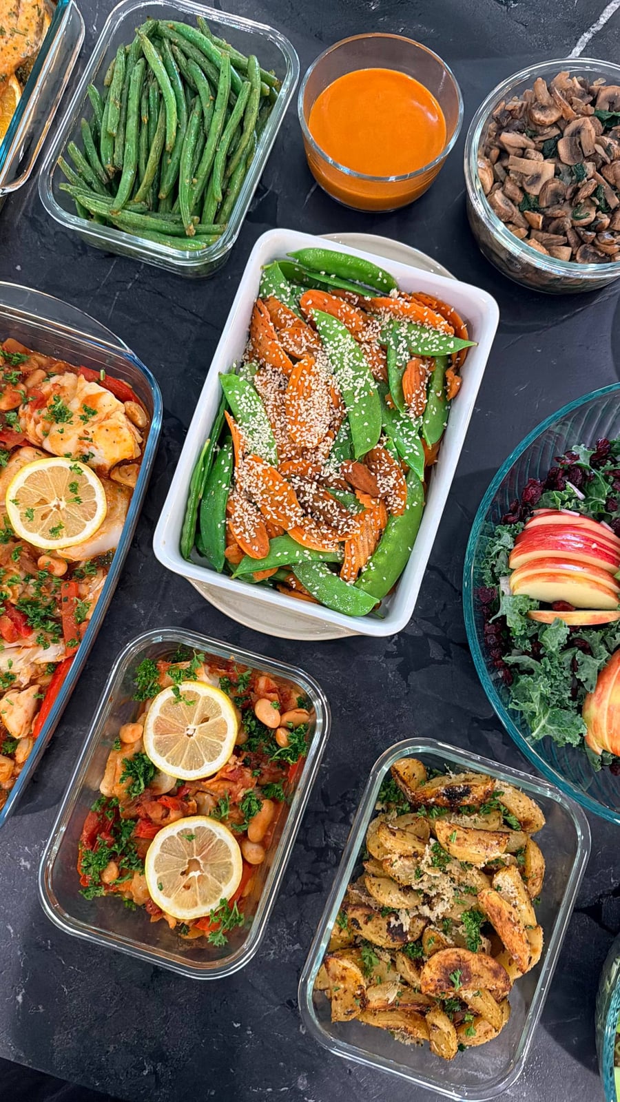 A collection of gourmet meal prep dishes including carrot and snow pea stir fry, barramundi, herb-baked potato wedges, and kale salad in glass containers.