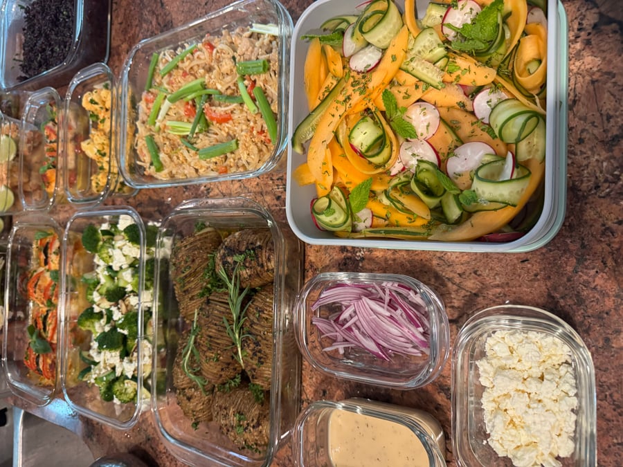 A variety of glass containers filled with hasselback potatoes, pad thai, broccoli zucchini, and melon cucumber salad, all neatly arranged for easy service.