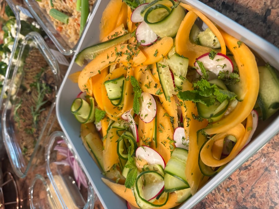 A square dish features a refreshing melon cucumber radish salad with mint, arranged in glass containers, displaying vibrant colors and artistic ribboned vegetable carvings.