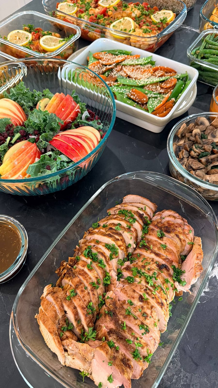 A glass serving dish containing sliced paprika-baked pork tenderloin garnished with chopped parsley, served with a side of rustic mango dipping sauce.