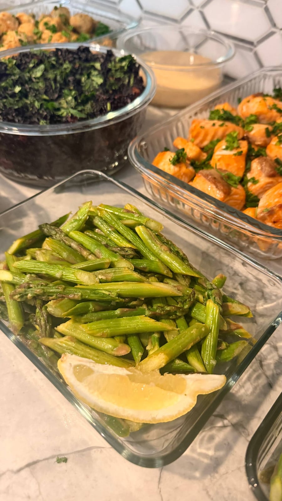 Glass meal prep containers filled with garlic salmon bites, cilantro almond black rice, and ginger garlic asparagus stir-fry garnished with a fresh lemon wedge.
