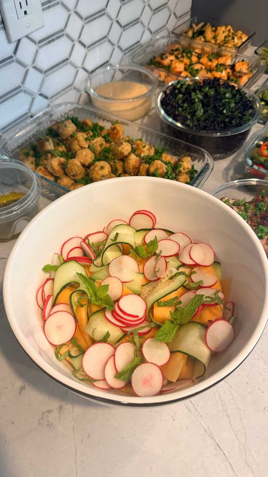 A large white bowl filled with a refreshing melon, cucumber, and radish salad garnished with sprigs of fresh mint and a light lemon vinaigrette dressing.