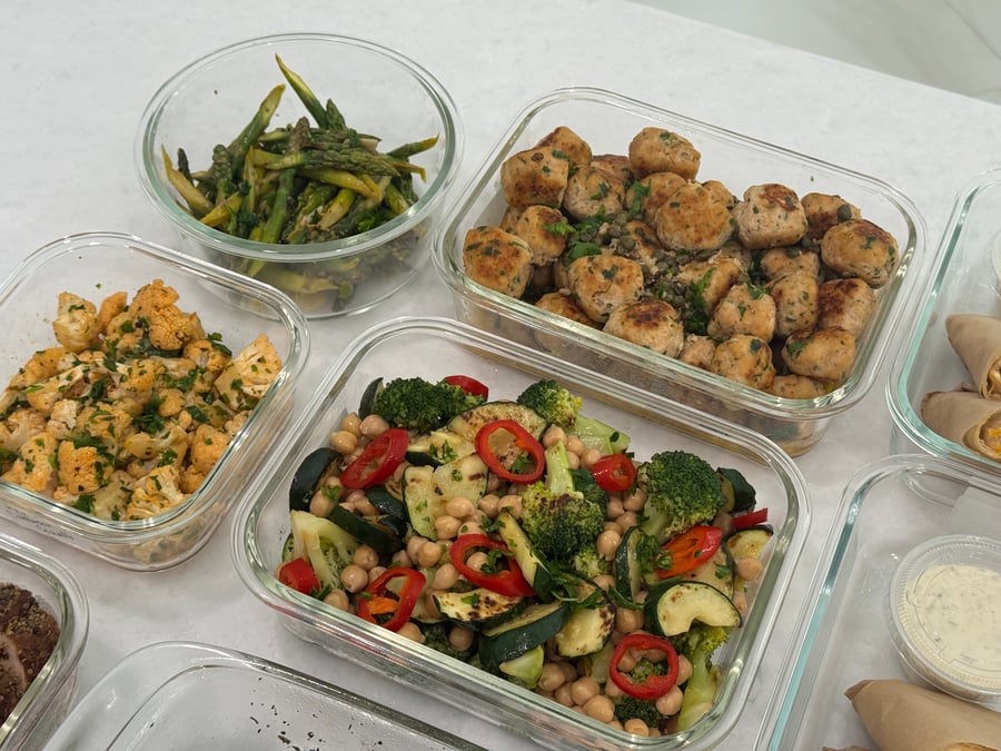Glass meal prep containers filled with chicken piccata meatballs, ginger asparagus, honey lime cauliflower, and chili seared broccoli with chickpeas and zucchini.