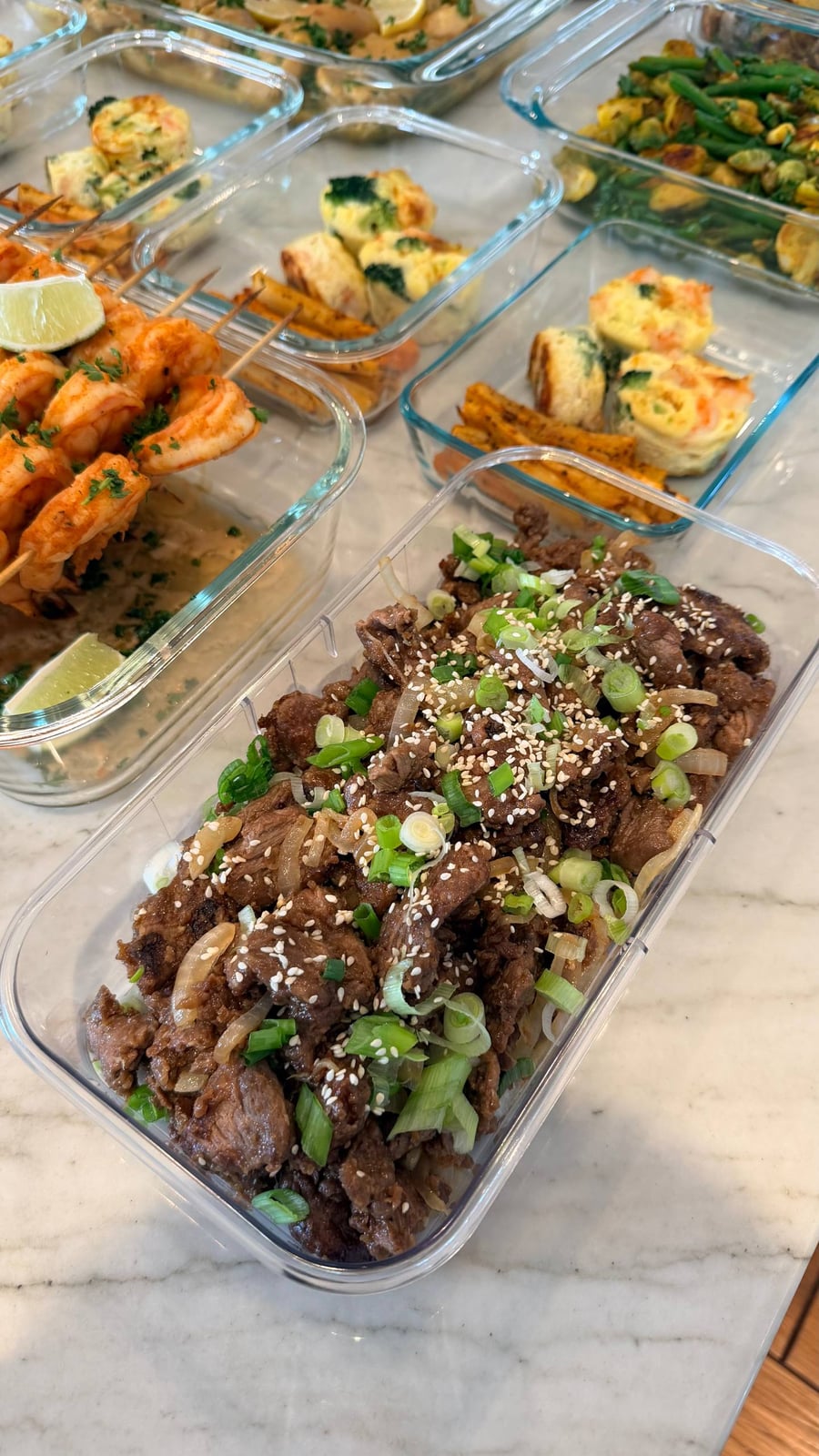 A glass meal prep container filled with tender Chinese beef and onion stir fry, garnished with toasted sesame seeds and fresh sliced green onions.