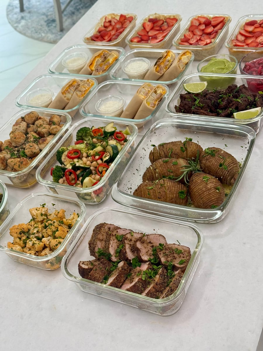 A variety of glass meal prep containers featuring shredded beef, pork tenderloin, chicken meatballs, strawberry baked oats, and vegetable sides on a counter.