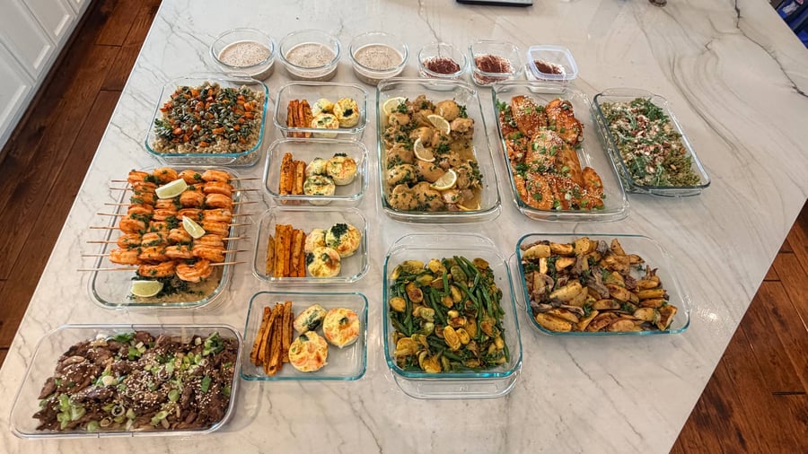 A variety of glass meal prep containers featuring shrimp skewers, honey garlic chicken, beef stir-fry, omelette bites, roasted vegetables, and tiramisu overnight oats.