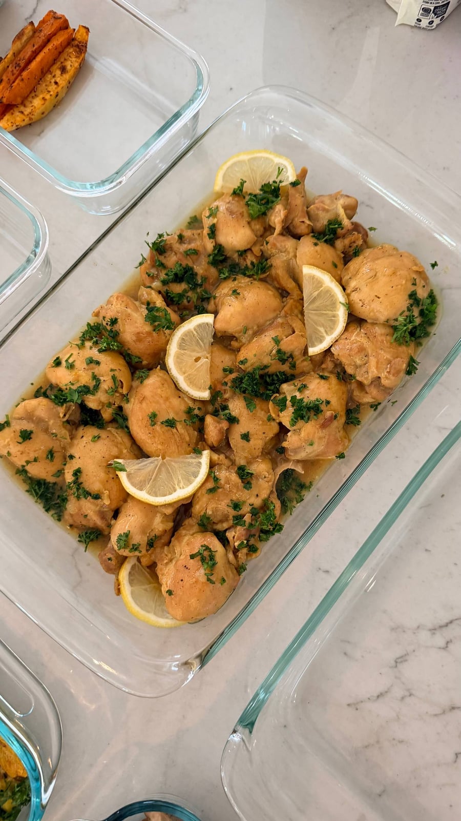 A large glass dish filled with golden saffron turmeric baked chicken thighs garnished with fresh lemon slices and finely chopped green parsley.