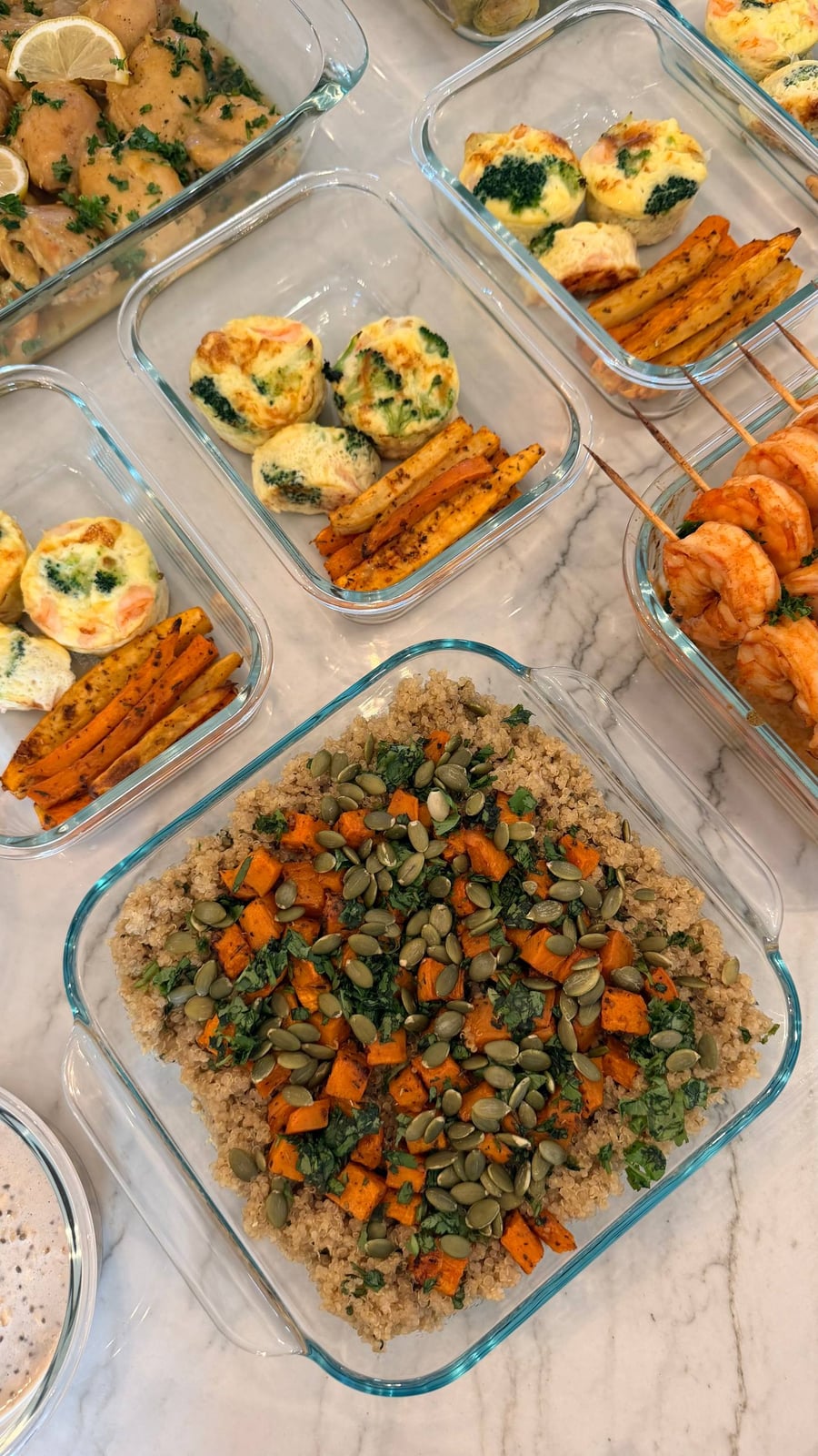 Glass containers featuring shrimp broccoli omelets, roasted sweet potato bites, paprika lime shrimp skewers, roasted sweet potato cilantro quinoa, and saffron turmeric chicken.