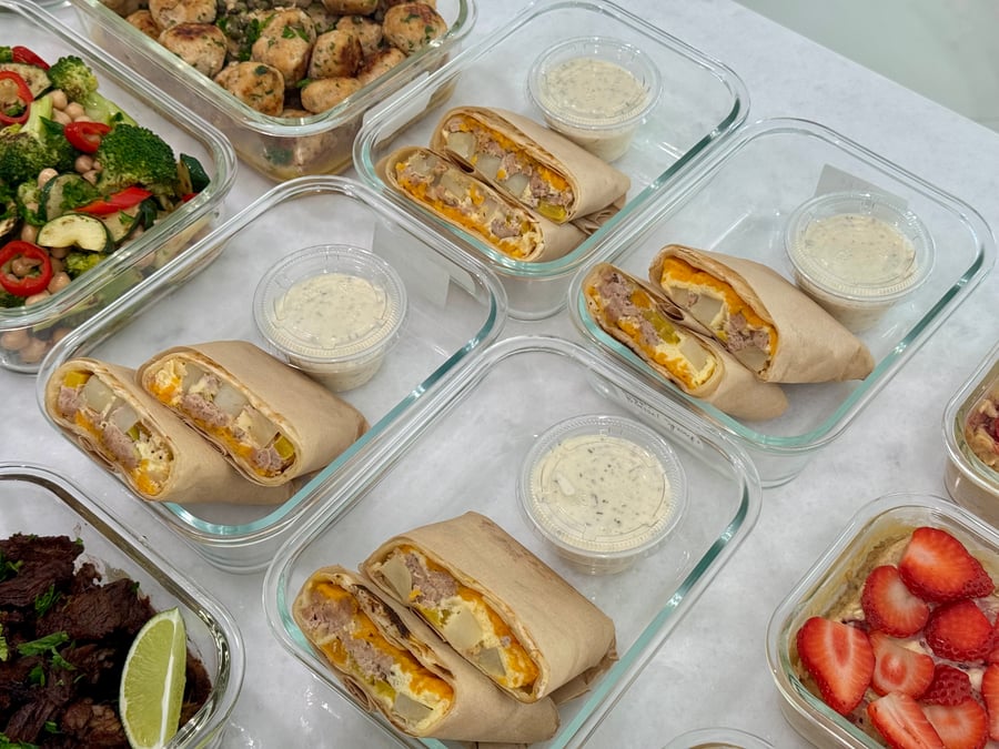 Glass meal prep containers each holding two halves of a turkey and egg breakfast burrito with a side of creamy ranch dipping sauce.