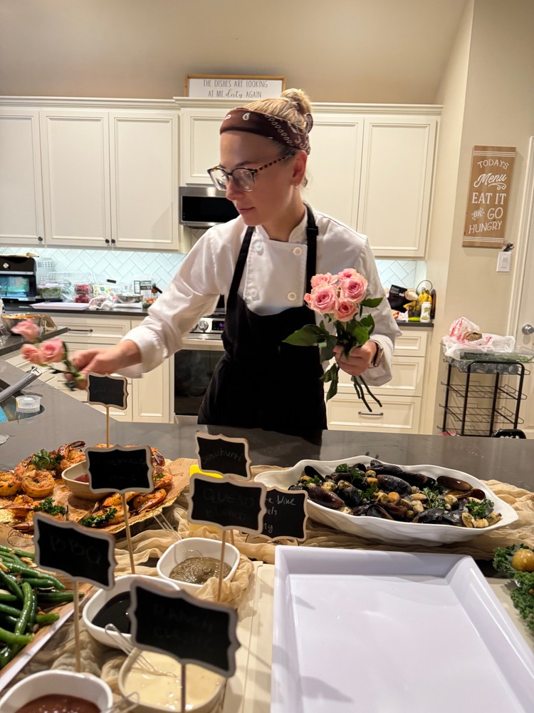 Chef Ana placing a pink rose on the buffet table next to a sauce