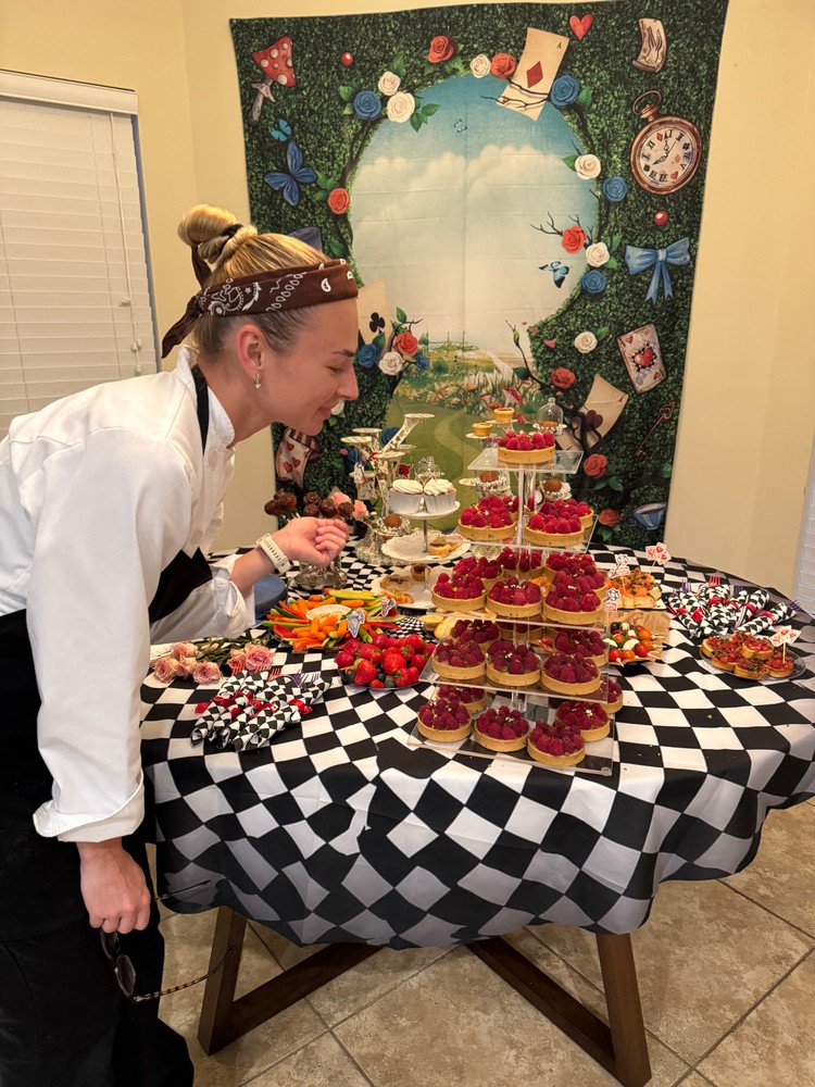 Chef Ana arranging a dessert display with mini raspberry tarts and cupcakes