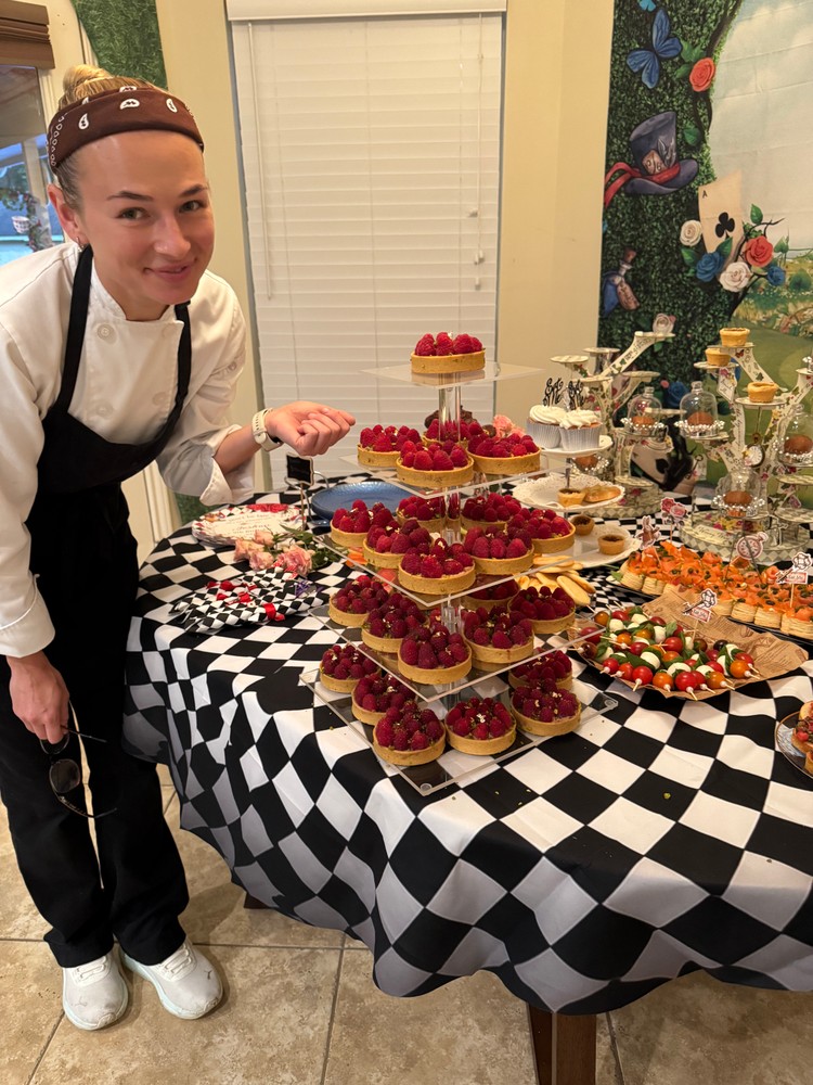 Chef Ana smiling next to a dessert table with raspberry tarts and fruit skewers
