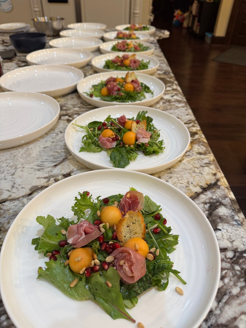 Multiple plates of fresh salad with prosciutto, melon, pomegranate, pine nuts, and croutons.